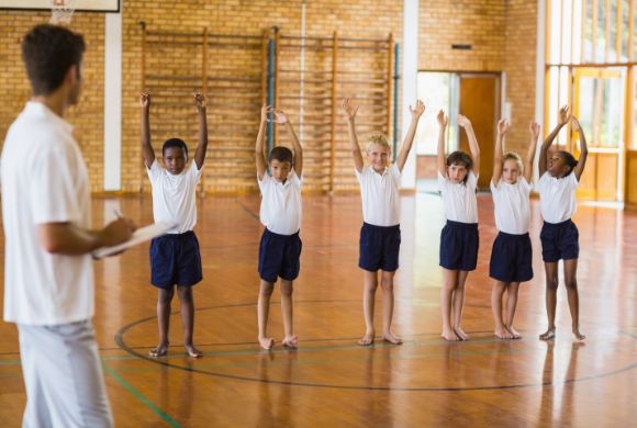 teacher with clipboard watching pupils doing jumping jacks